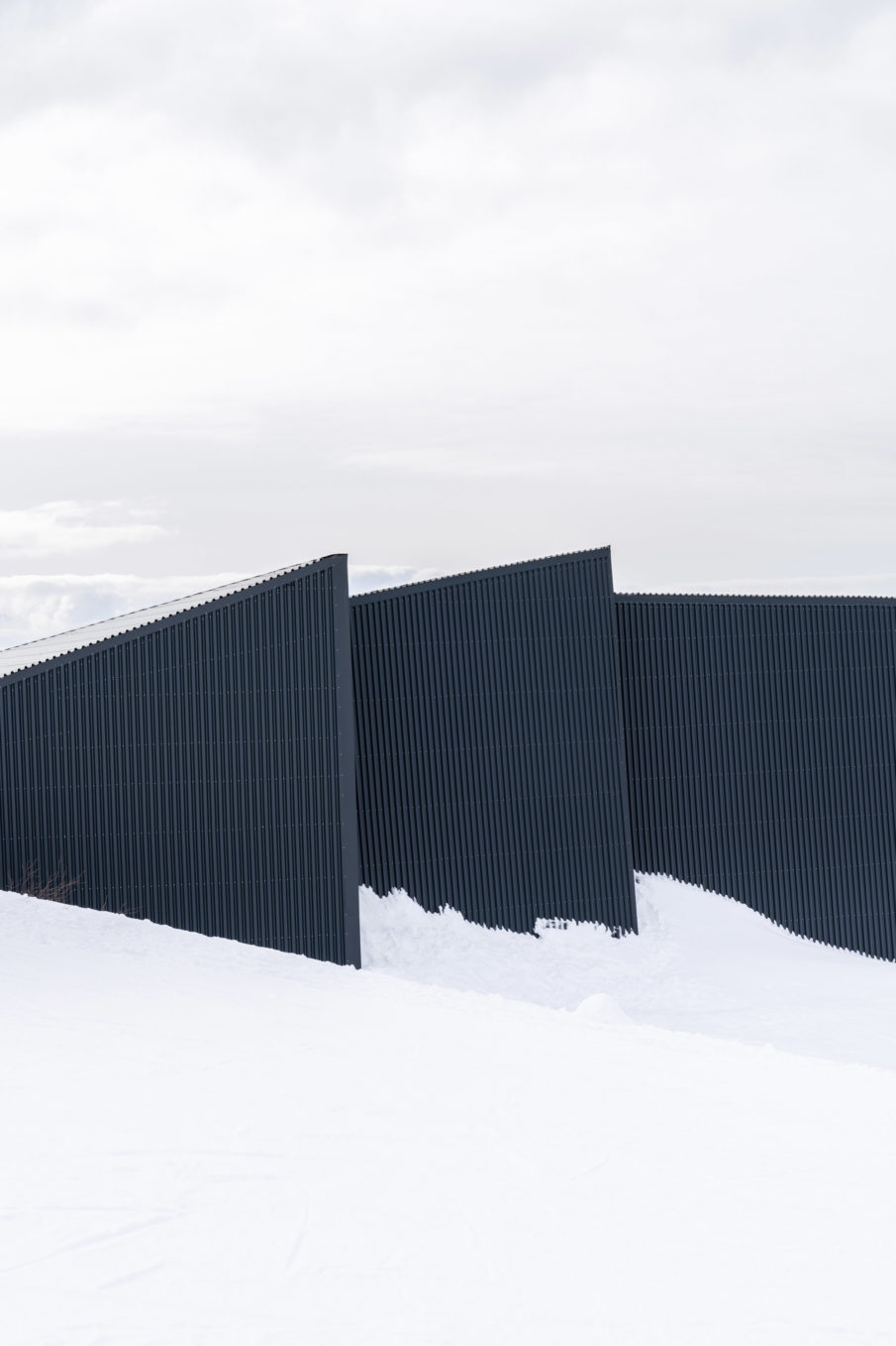 The exterior of a modern cabin in black contrasting with the white snow.