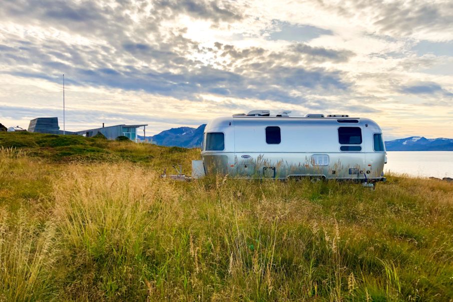 A caravan placed next to a cabin with a view of the sea and mountains on a sunny day.