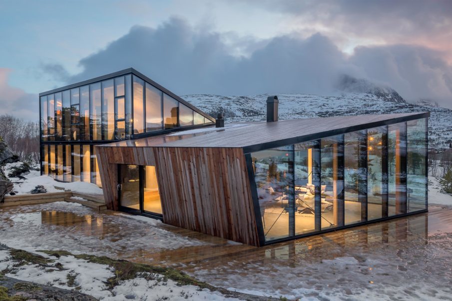 A house with numerous large windows overlooking the mountain on the other side during winter.