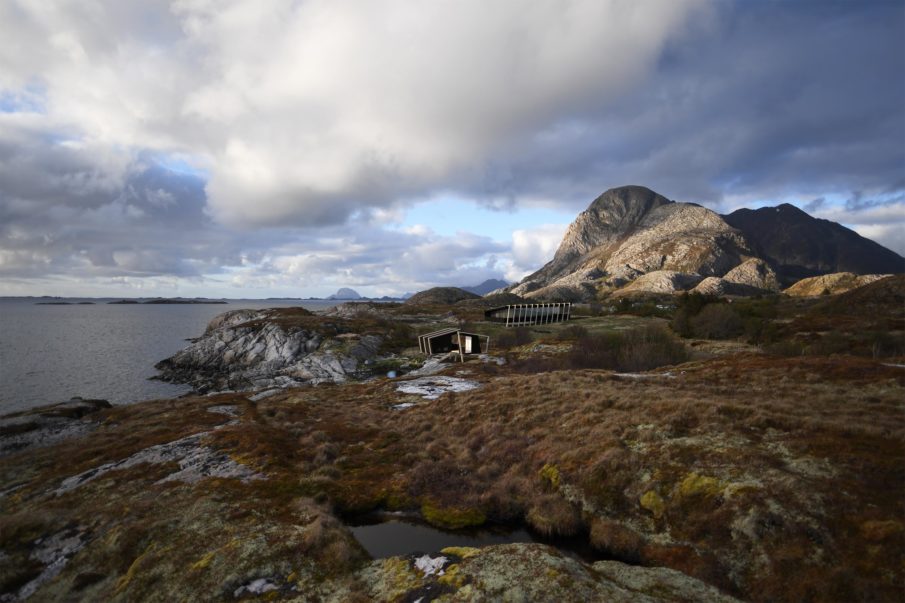 View of two cabins in the midst of nature, surrounded by mountains and water.