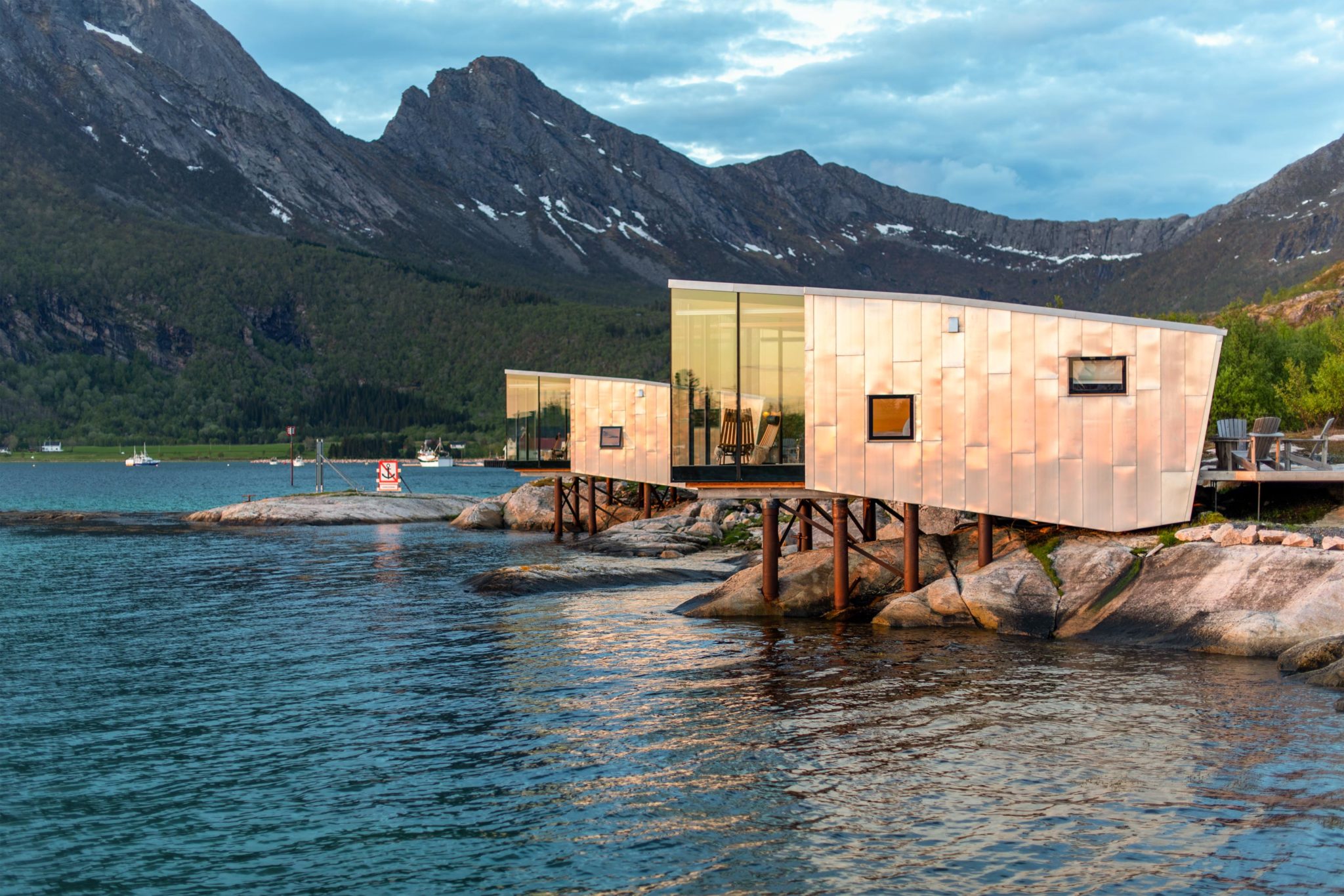 Two modern cabins built on support pillars from the mountain, overlooking water and mountains.